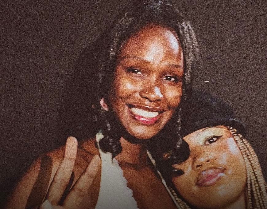A guest in a white top smiling as a friend in a dark cap leans on her shoulder