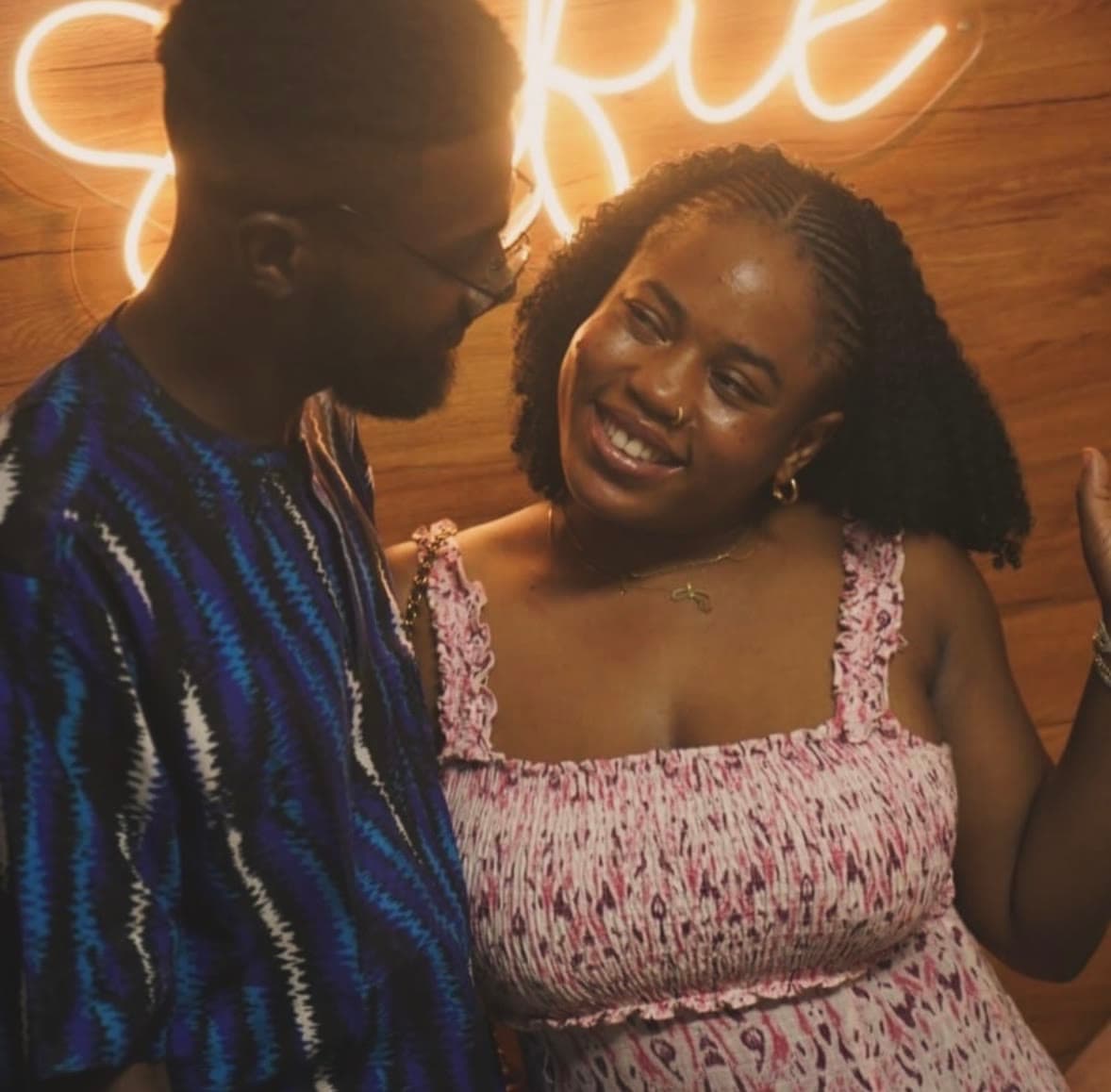 Two friends laughing together in front of a glowing neon sign